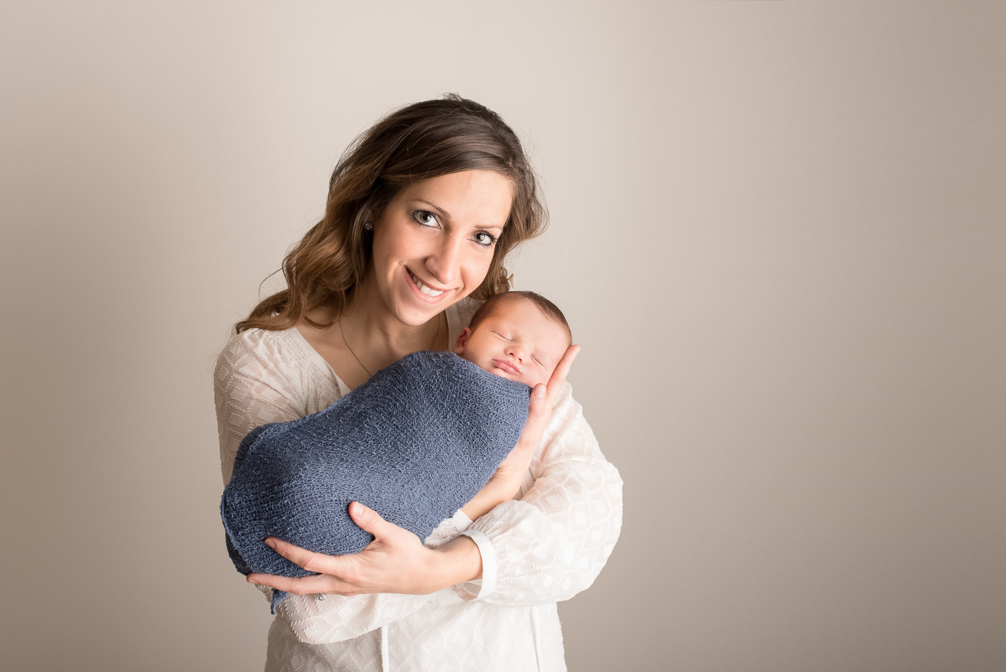 mom in white top holds newborn son in a blue wrap during a posed studio newborn portrait session in Pittsburgh, PA photography