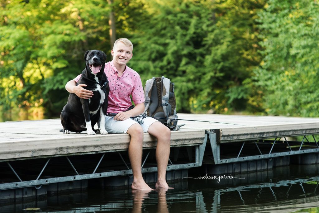 senior boy sits with his dog on a dock for senior portraits in Bethel Park PA