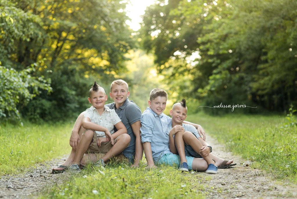 four boy siblings sit in the green grass for family portraits